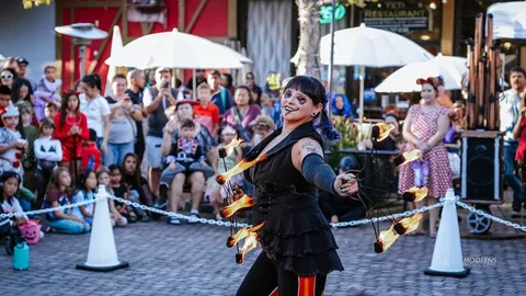 A fire dancer spins glowing poi through the air on a crowded downtown street.