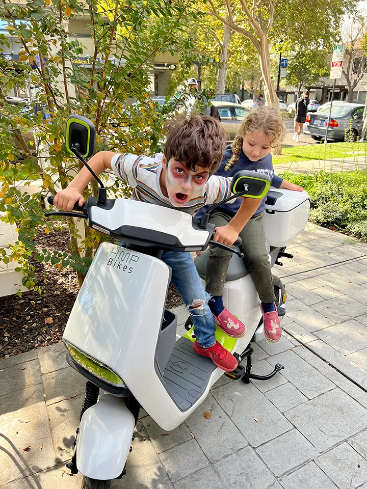 A close view of two people's legs on a step-through electric scooter.