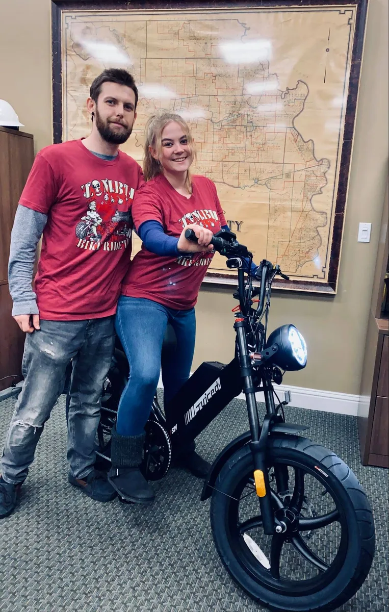 A couple in matching festival shirts poses together on an electric bike.