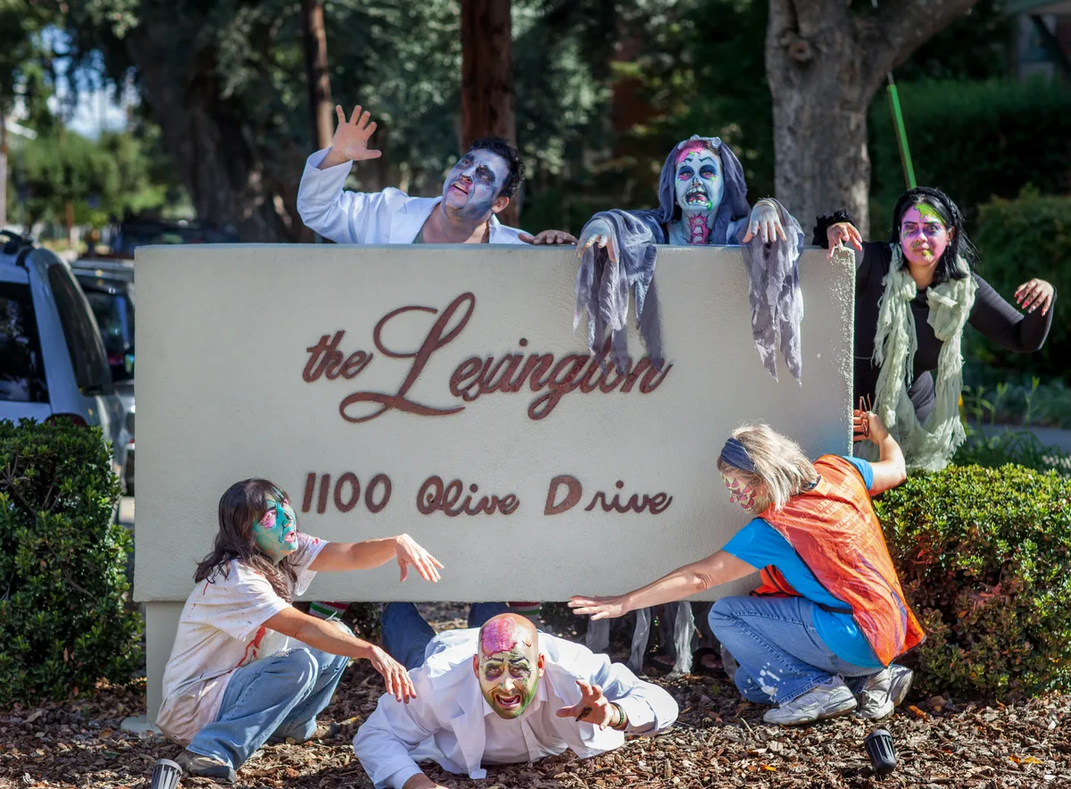 Two zombie-costumed women pose beside The Lexington apartment community sign.