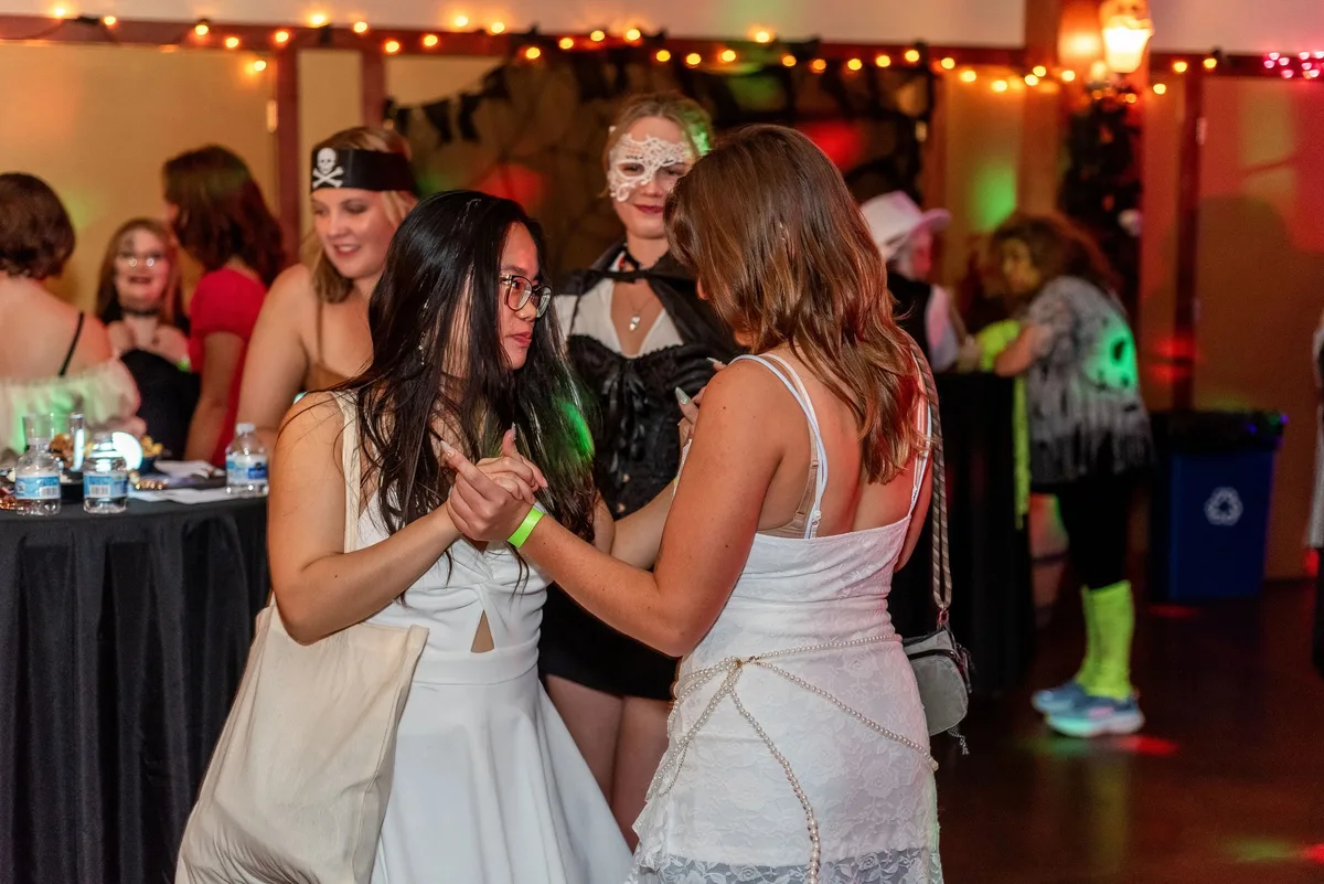 Guests in white costumes dance together under string lights at the Zombie Ball.