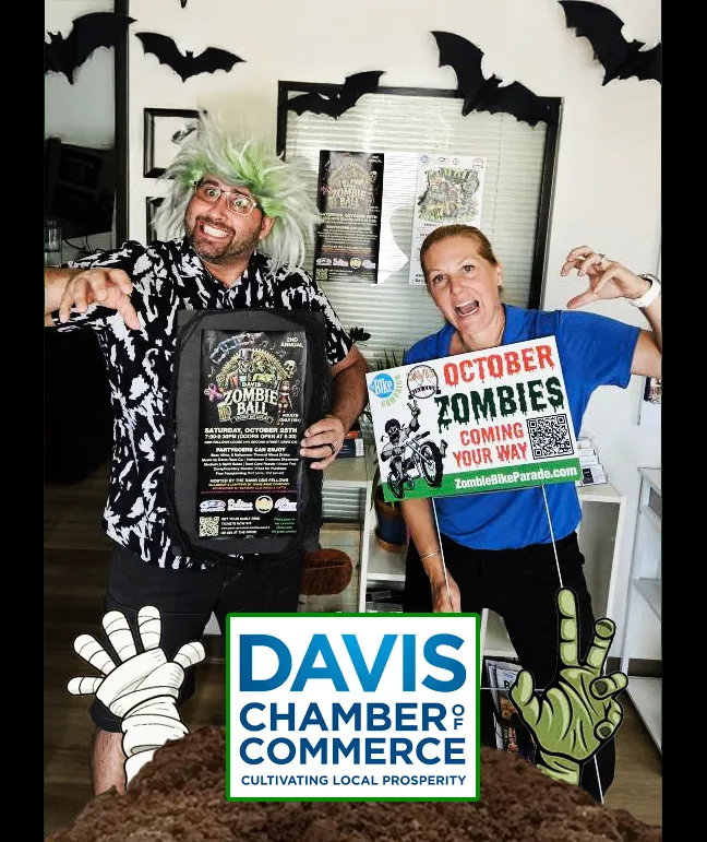 Two people pose with a Davis Chamber of Commerce sign indoors.