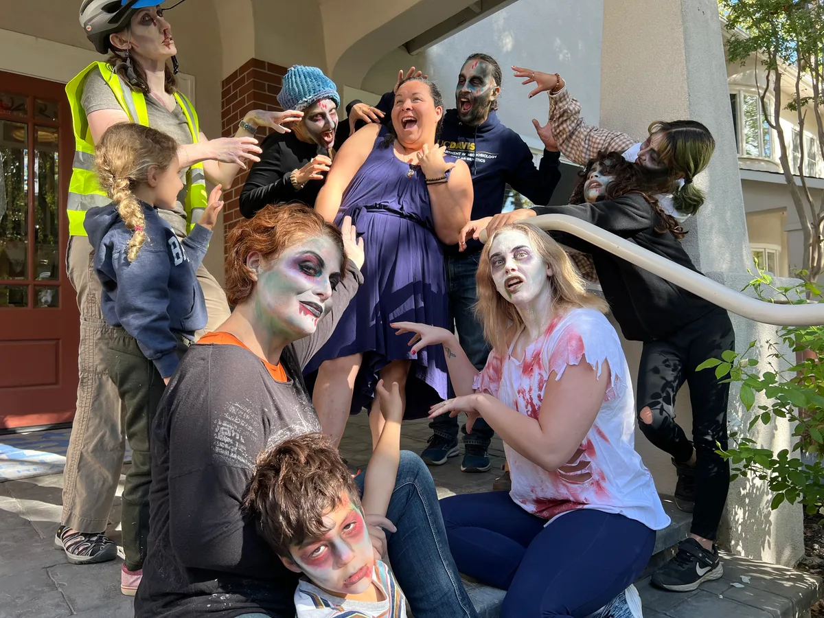 A group of adults and children in zombie makeup pose lunging at the camera on the steps of a house.