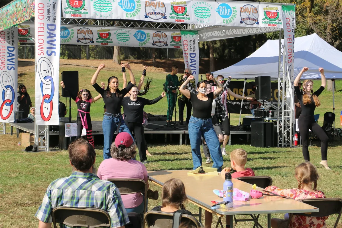 A group dances together on an outdoor festival stage.