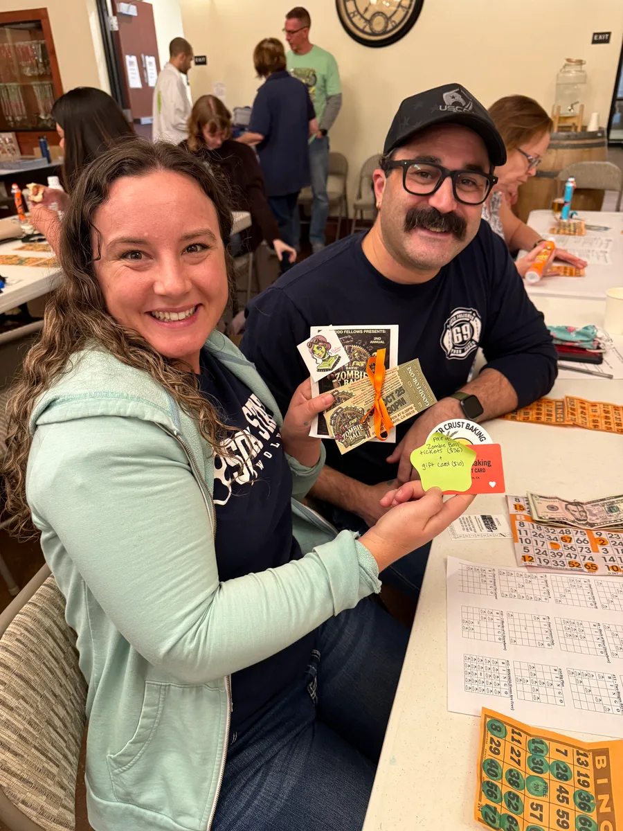 A man and woman smile together holding festival cards indoors.