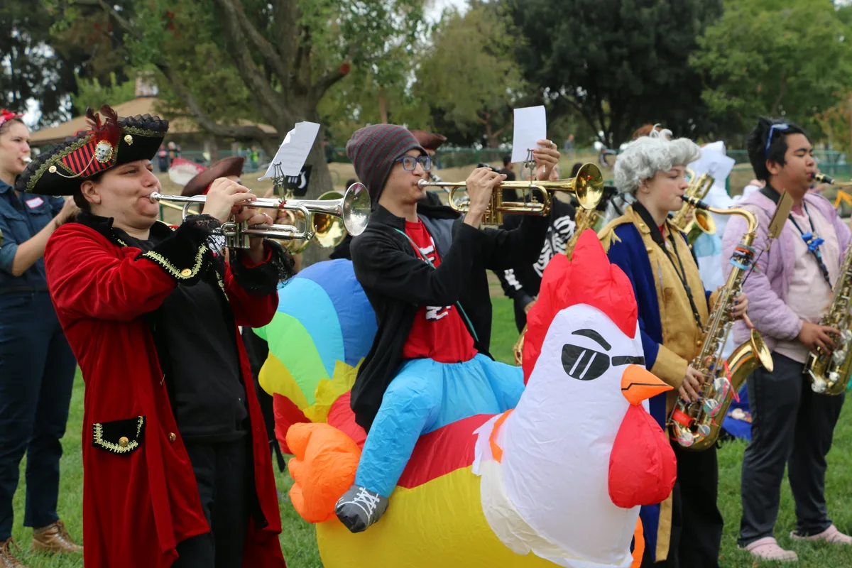 A costumed marching band plays horns beside a giant inflatable chicken in the parade.