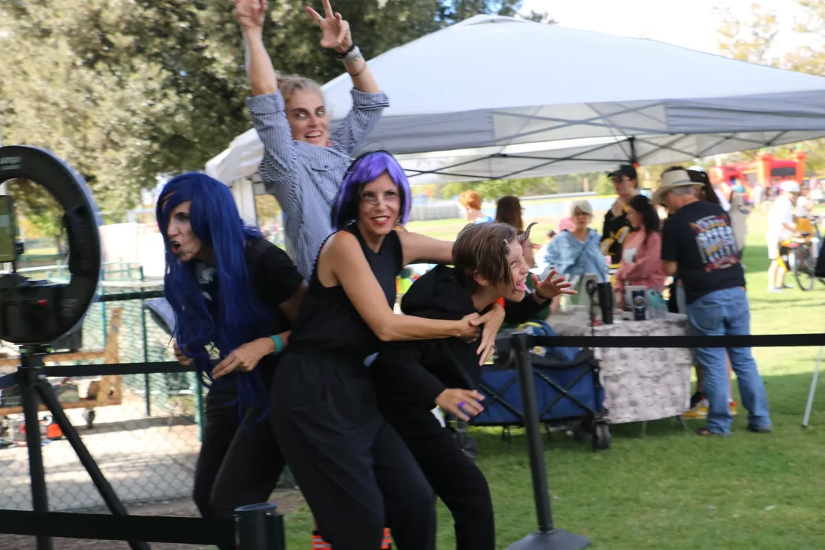 Two people in colorful wigs and zombie makeup pose outdoors near a tent.