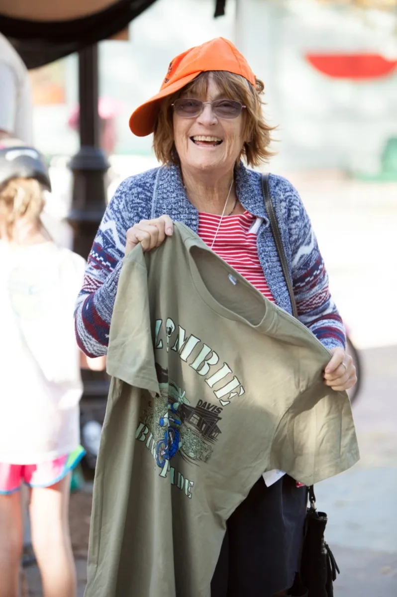 A woman in an orange sun hat smiles on a downtown street.