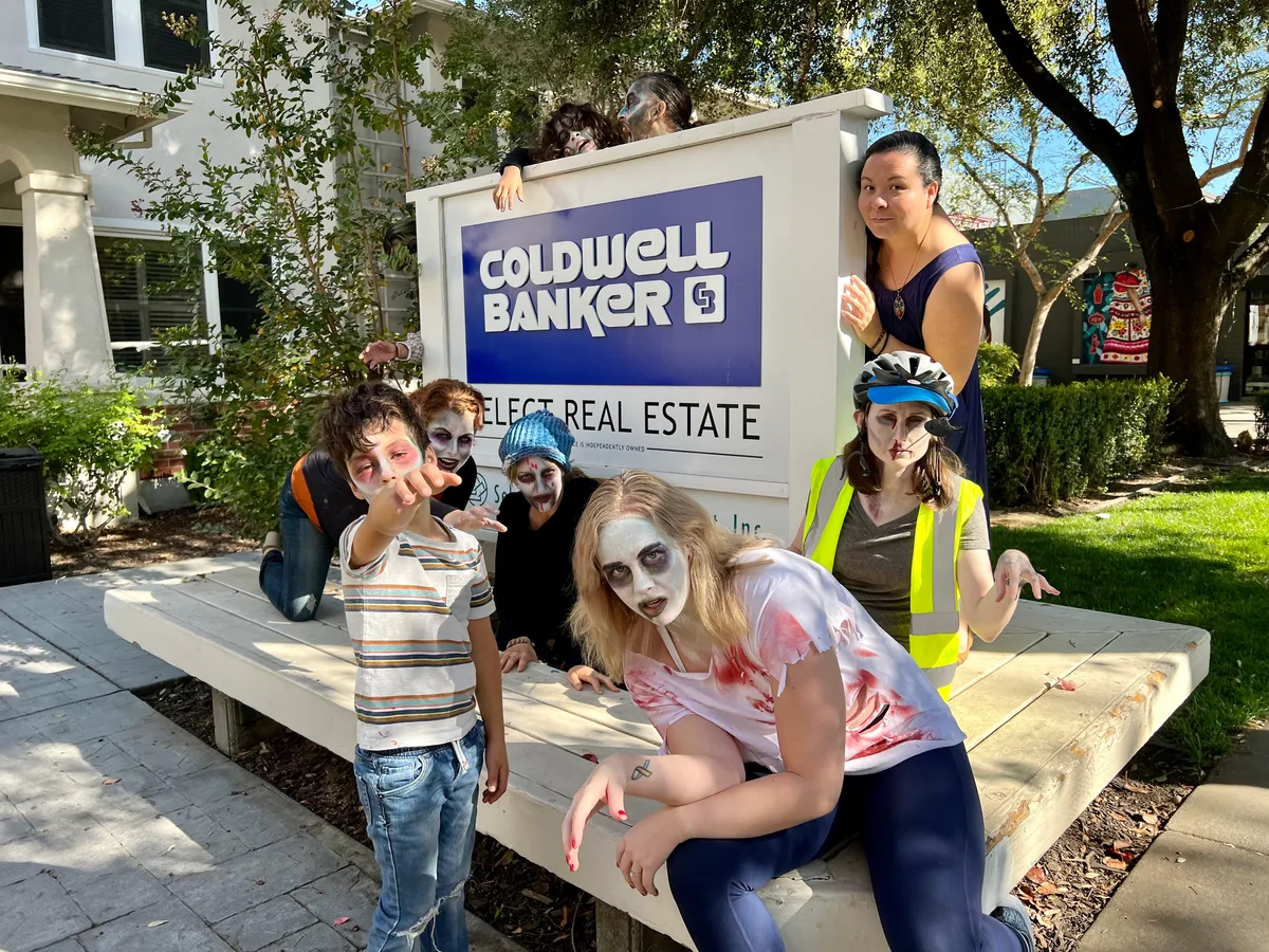 A costumed group poses in front of the Coldwell Banker sign.