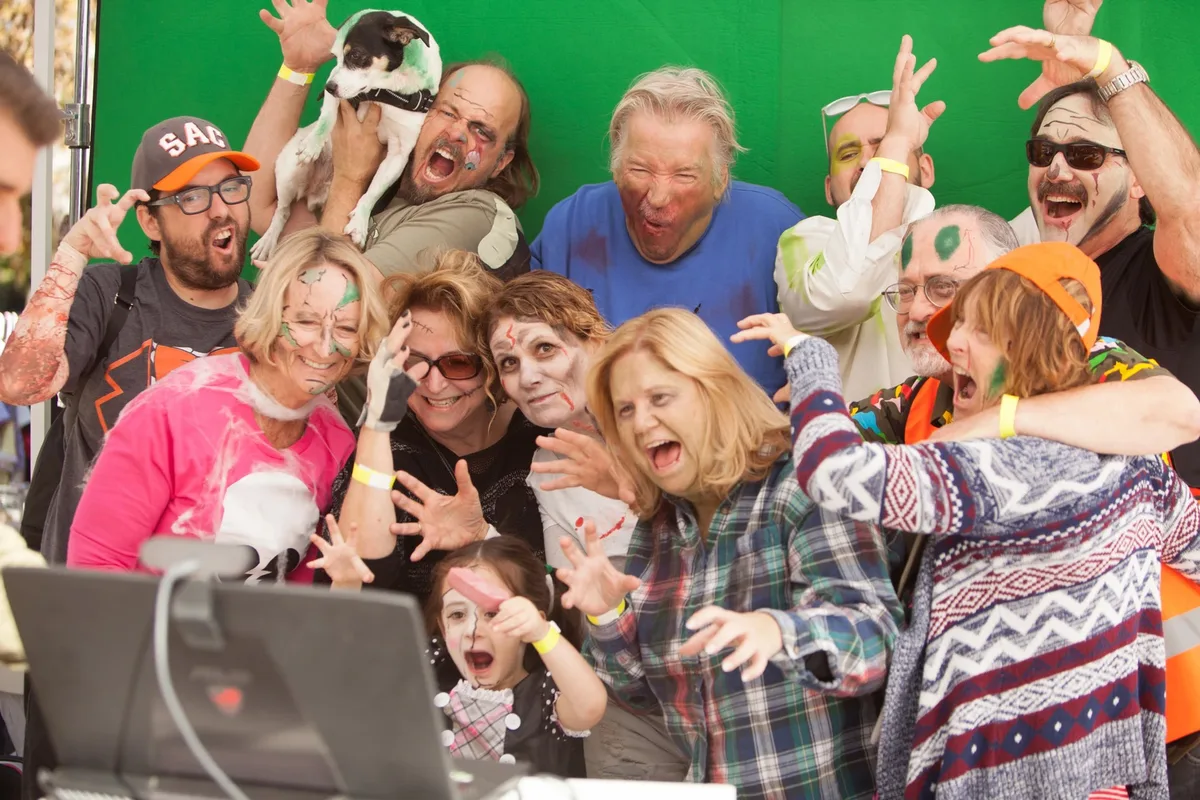 A costumed group and a dog take a playful selfie against a green screen.