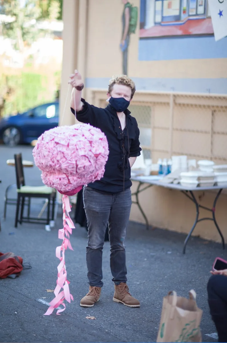 A volunteer holds up a large pink brain pinata with ribbon streamers outside the Davis Arts Center.