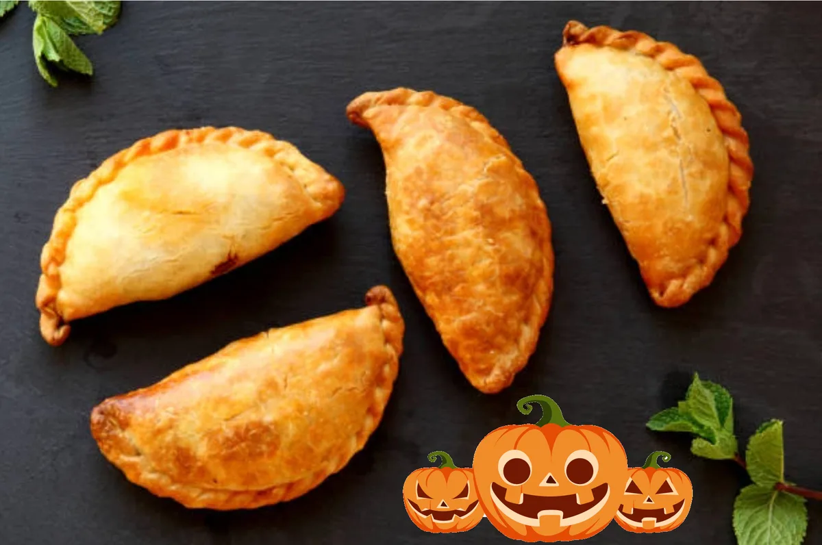 Golden fried empanadas are arranged next to small pumpkin decorations.