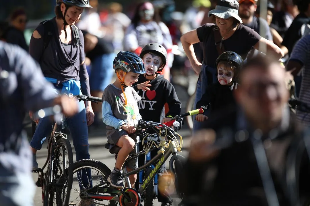 A child with face paint rides a bike at the front of a crowd of cyclists.