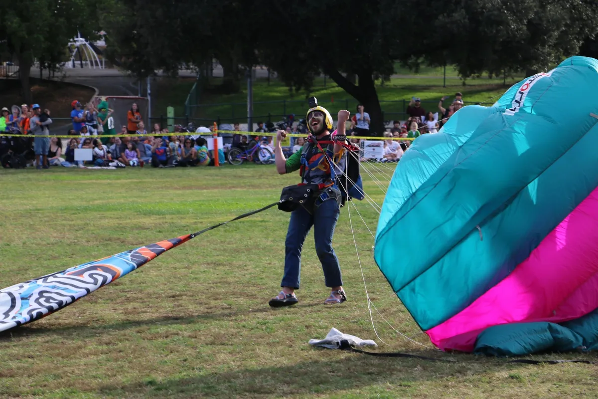 Two people gather a large teal parachute on the ground after landing.