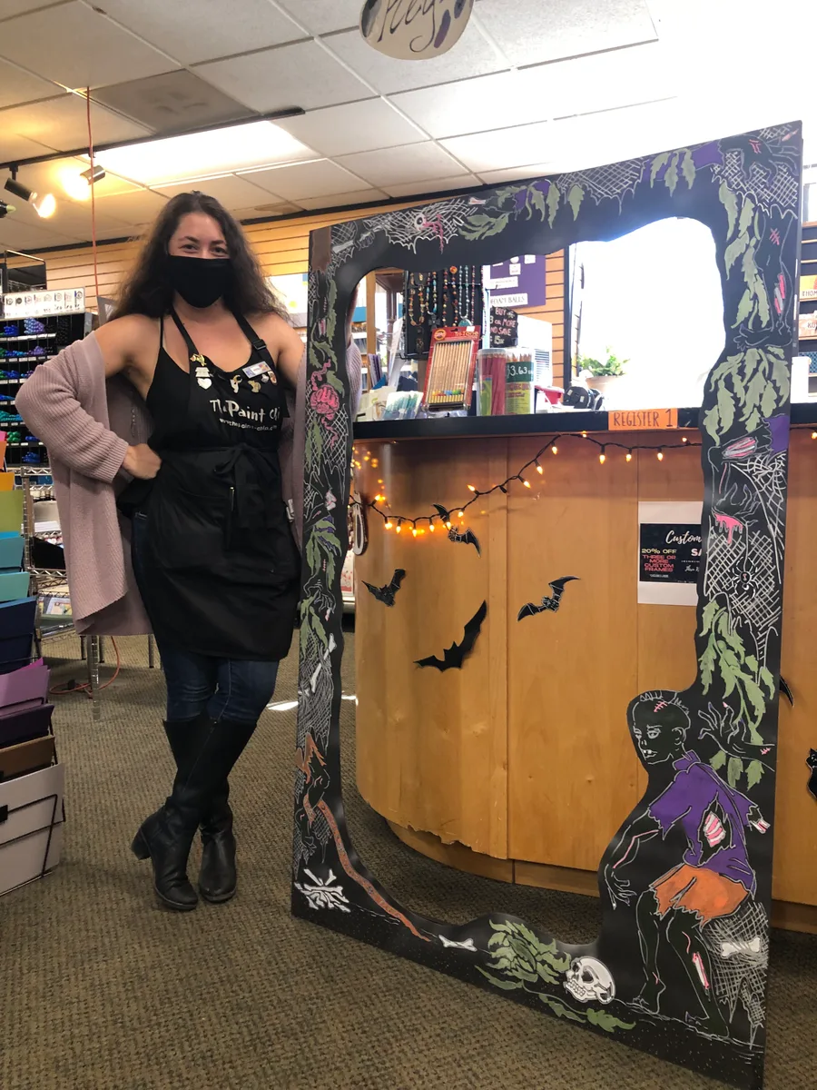 A woman stands at a shop entrance decorated with bats and spooky decor.