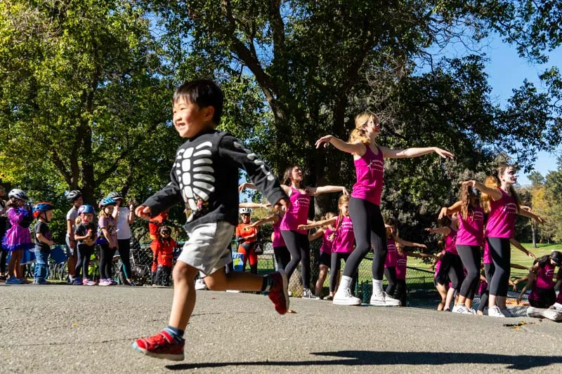 Children in skeleton costumes dance together on the sidewalk.
