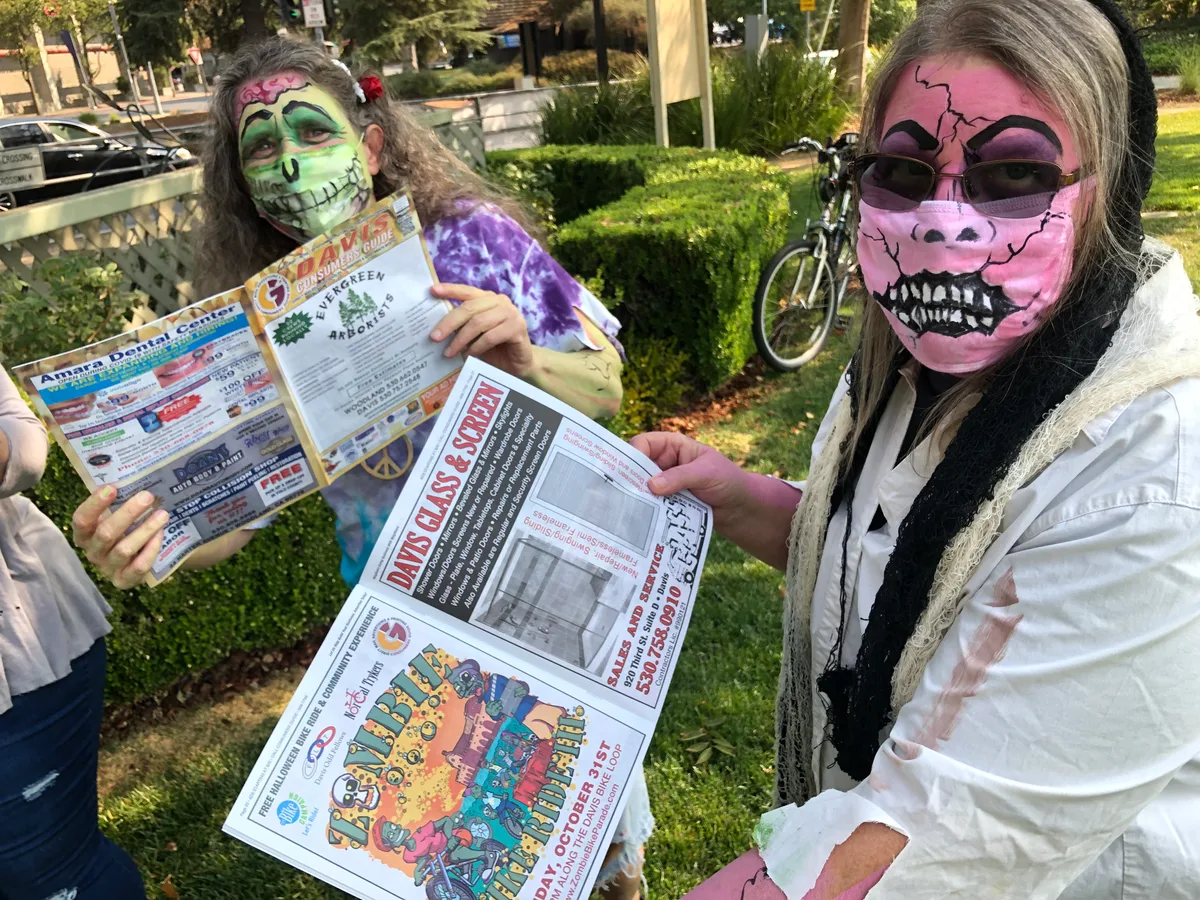 Two women in zombie makeup hold up festival guide flyers.