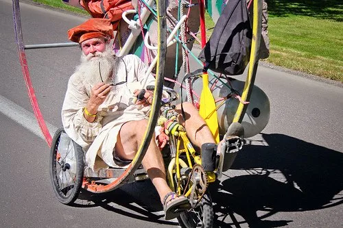 A costumed rider pedals an elaborate homemade parade bike decorated with flags.