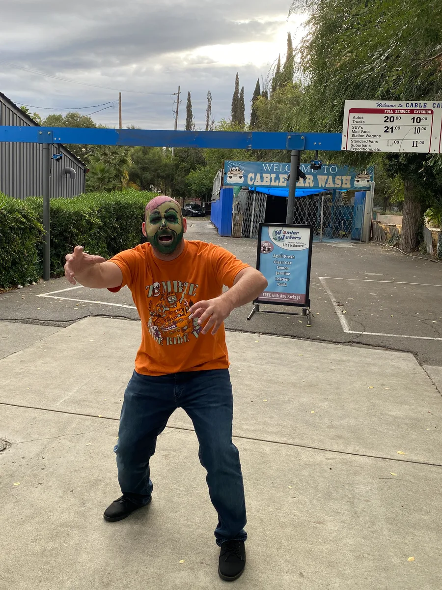 A man in an orange shirt strikes a martial-arts pose in an empty lot.