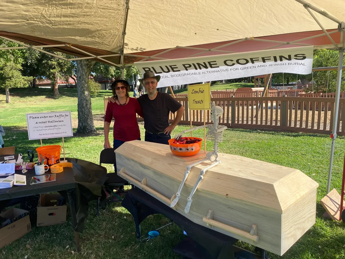 Two people pose beside a prop coffin at the Blue Pine Coffins booth.