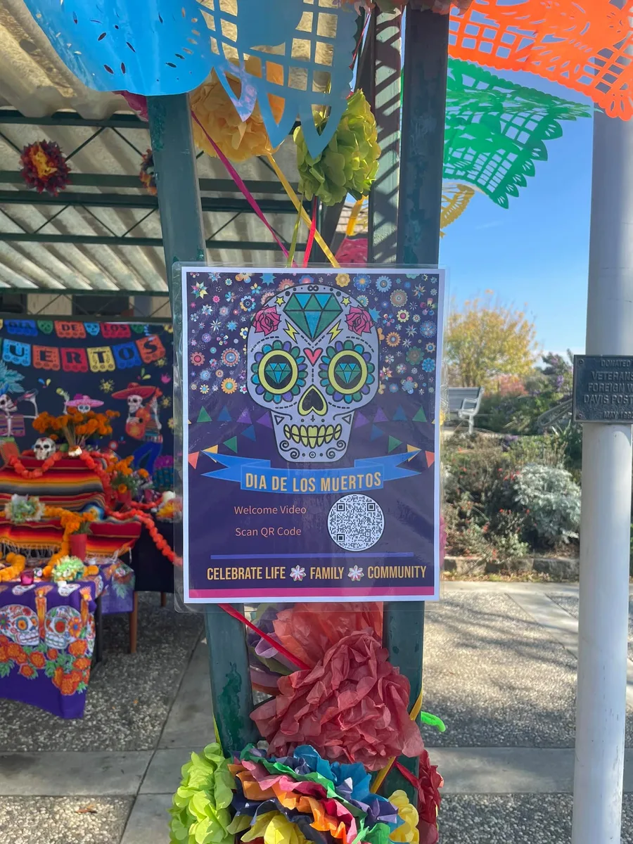 A colorful Dia de los Muertos community altar display sits outdoors.