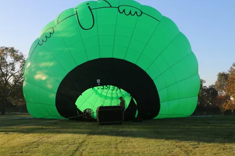 A giant green hot air balloon forms a dark tunnel as a worker inflates it at sunrise.