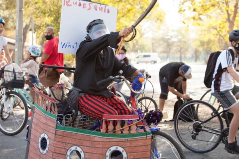 A rider dressed as a pirate raises a sword atop a handmade cardboard pirate-ship bike float.