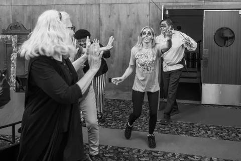 Black and white: a zombie in skull makeup runs down the hallway with her arms out as two people throw their hands up in front of her.