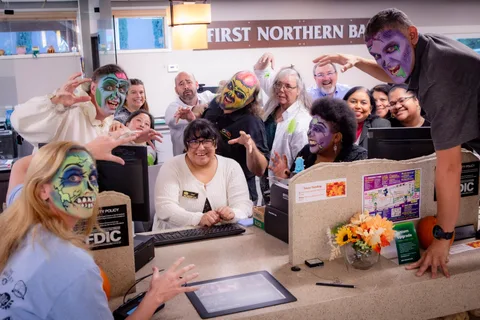Bank staff and zombies crowd behind the teller counter at First Northern Bank, grinning and reaching forward over the desk.