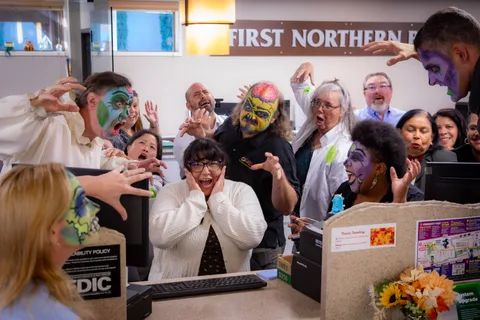 A teller clutches her face and screams for the camera as a dozen zombies loom over the counter behind her at First Northern Bank.