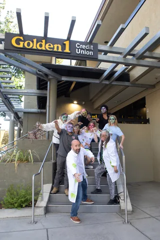 The zombie group posed on the Golden 1 Credit Union steps, arms outstretched, with the branch sign above them.