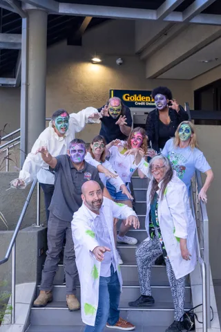 Nine people in zombie face paint crowd down the Golden 1 Credit Union steps towards the camera with their hands out.