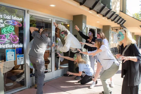 A wider frame of the same doorway scene, a line of zombies reaching towards the hall doors in the afternoon sun.
