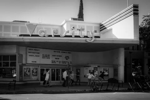 Black and white: a wide view of the Varsity Theatre with its neon sign, the group of zombies small along the sidewalk below.