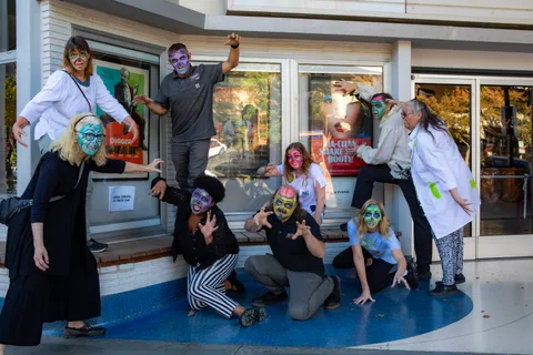 Nine zombies pose on the blue terrazzo outside the Varsity Theatre, some crouching, framed by the film posters in the lobby windows.