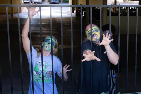 Two zombies press up against the black railings of a parking structure, reaching their hands through the bars.