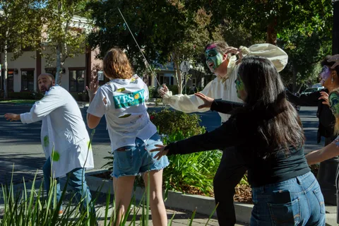 Zombies close in on a cyclist on a sunny street corner, one in a white pirate shirt holding a thin sword aloft.
