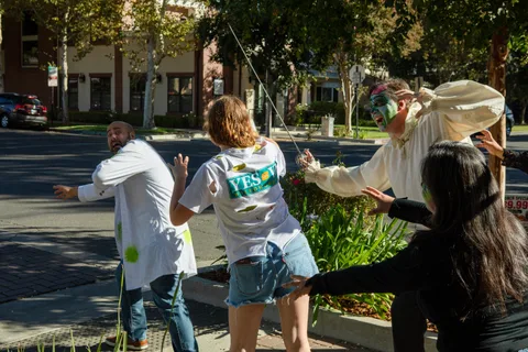 A wider frame of the same street corner, four zombies converging with their arms out while one holds a sword in the air.