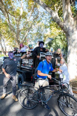 A cyclist in a helmet and blue polo shirt pedals away wide eyed while a trailer load of zombies reaches for him from a Junk Removal and Hauling truck.