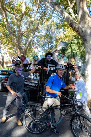 The same chase from a step back: nine zombies lean over the side of the black hauling trailer towards a cyclist in the street.