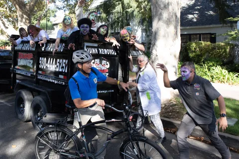 A wider frame of the trailer chase, the cyclist pushing off while zombies reach for him from the trailer and the roadside.