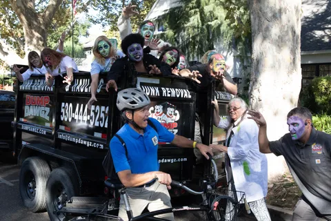 Close on the cyclist beside the Dump Dawgz trailer, zombies hanging over the rails above him and reaching in from the right.