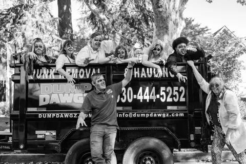 Black and white: the same trailer group portrait, a man in front throwing his arms wide while zombies lean over the rail behind him.