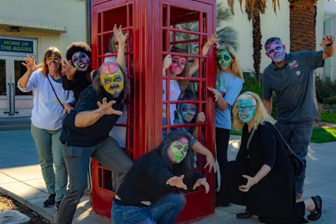 A tight group in bright zombie face paint crowd the red telephone box, some packed inside the glass and others lunging toward the camera.