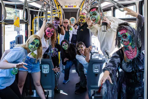 Zombies fill the aisle of a city bus, hanging from the grab handles and reaching toward the camera between the seats.