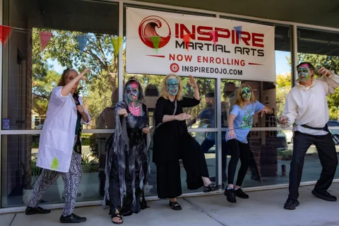 Five zombies strike loose martial arts poses under the Inspire Martial Arts banner, one in a lab coat and one in a grey shroud.