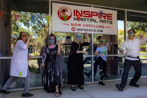 The group lines up in mock fighting stances along the studio windows beneath the Inspire Martial Arts banner.